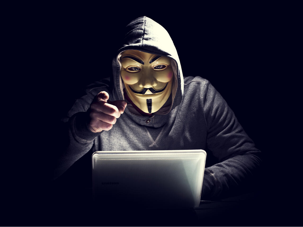 Hacker using a laptop Hacker wearing a Guy Fawkes mask using a laptop